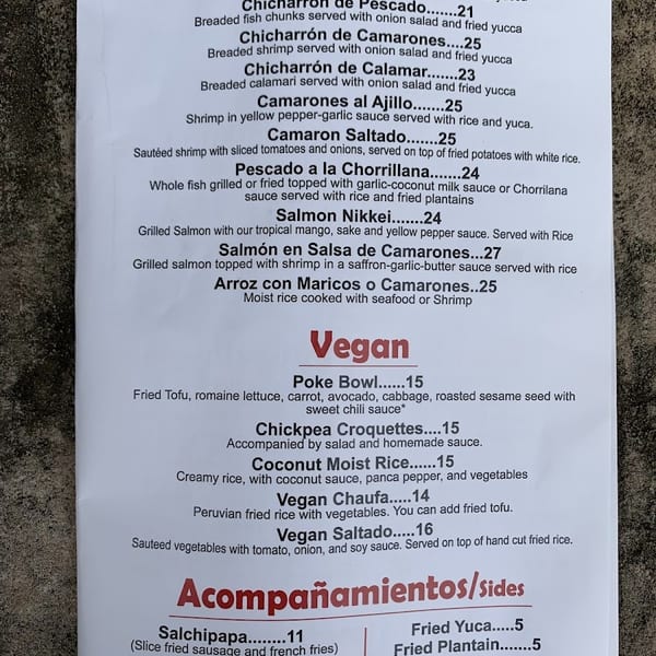 A white paper menu displays a variety of seafood, vegan, and side dishes with prices.
