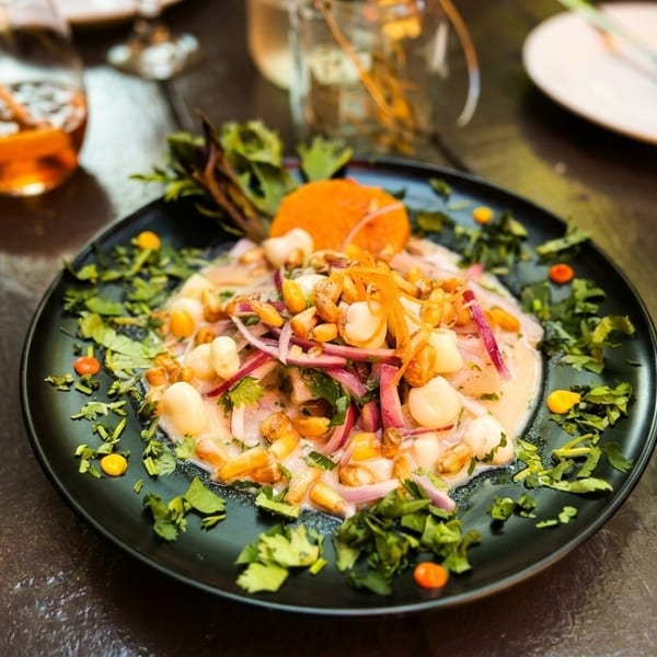 A vibrant ceviche dish with corn, red onion, and cilantro on a black plate.